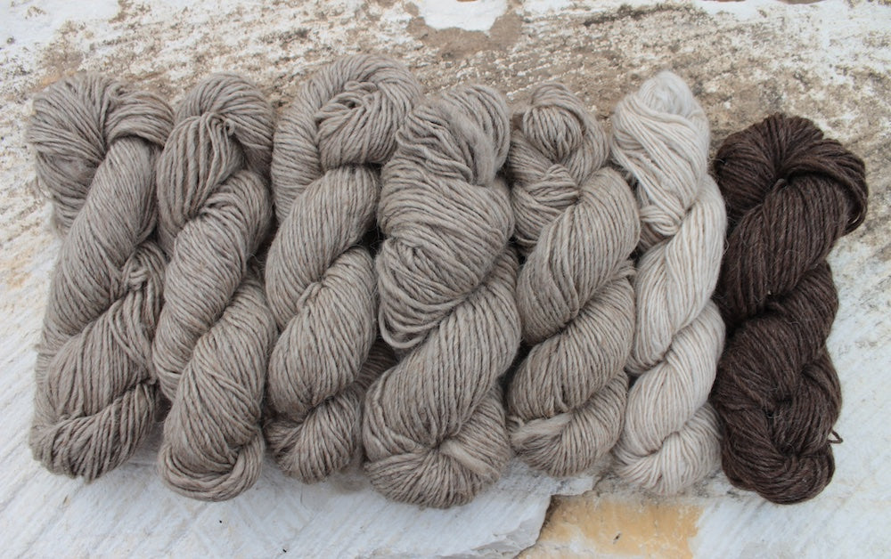 five skeins of slate, one of bone, and one of walnut laid out on a limestone background